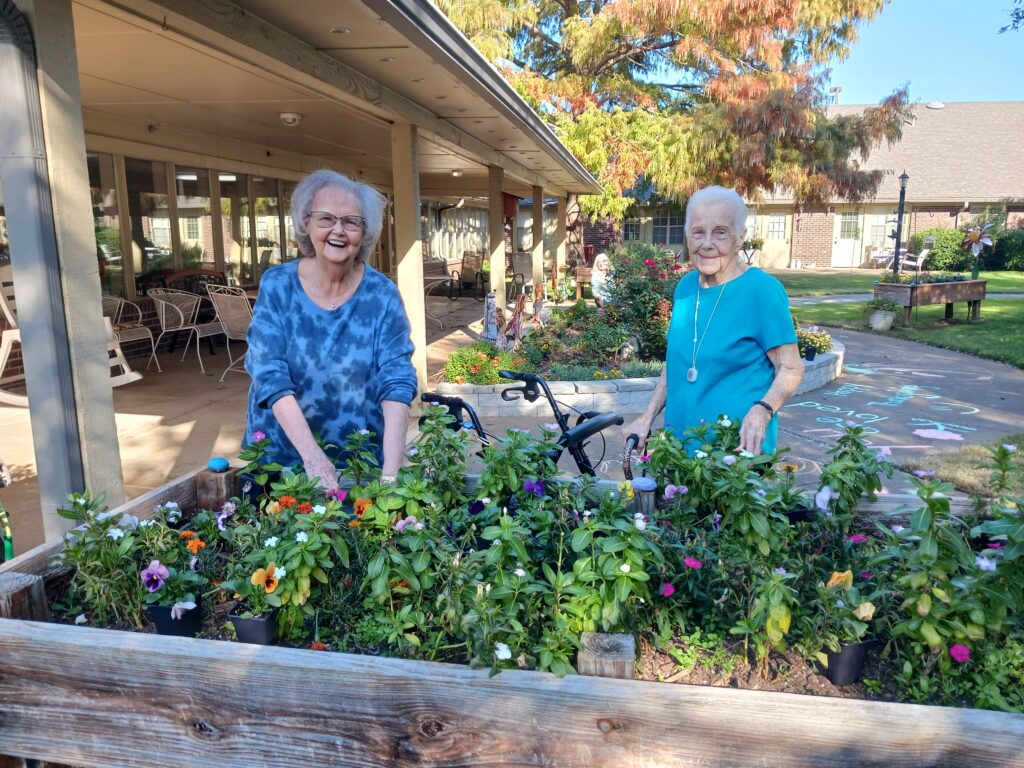 Two smiling residents gardening in a floral area.