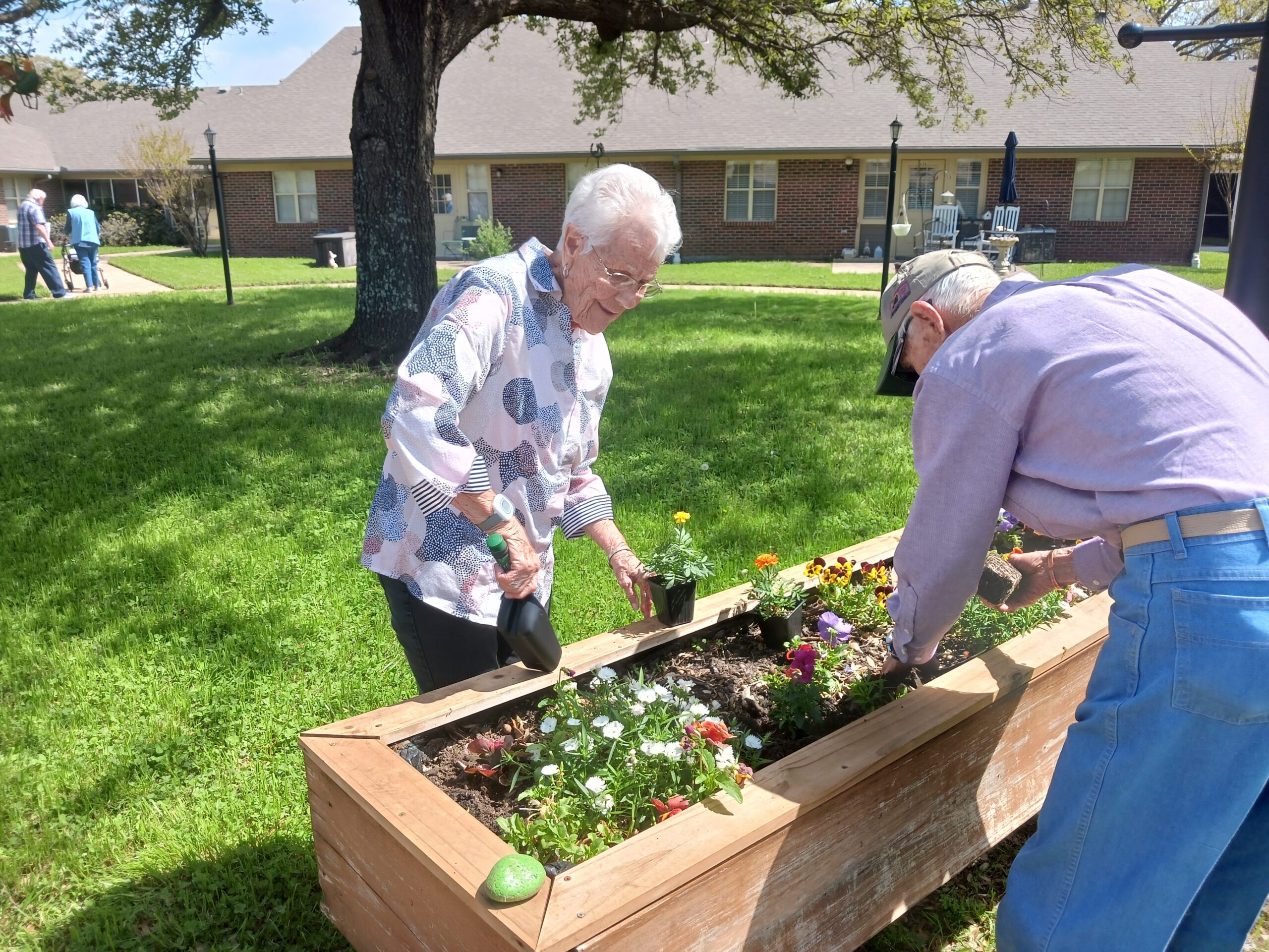 Residents gardening in a flowerbed outdoors.