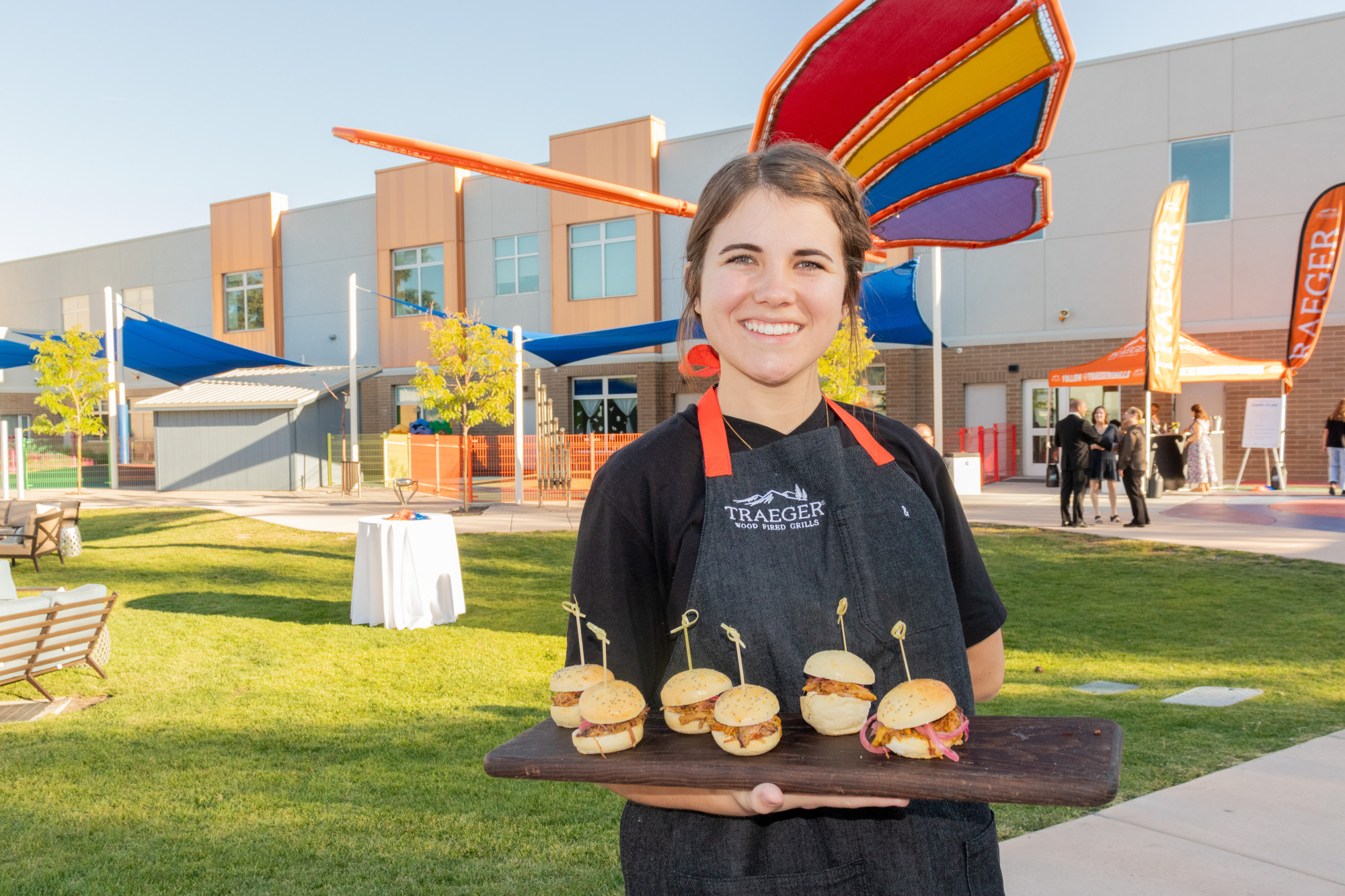 Cook presenting a platter of gourmet sliders outdoors.