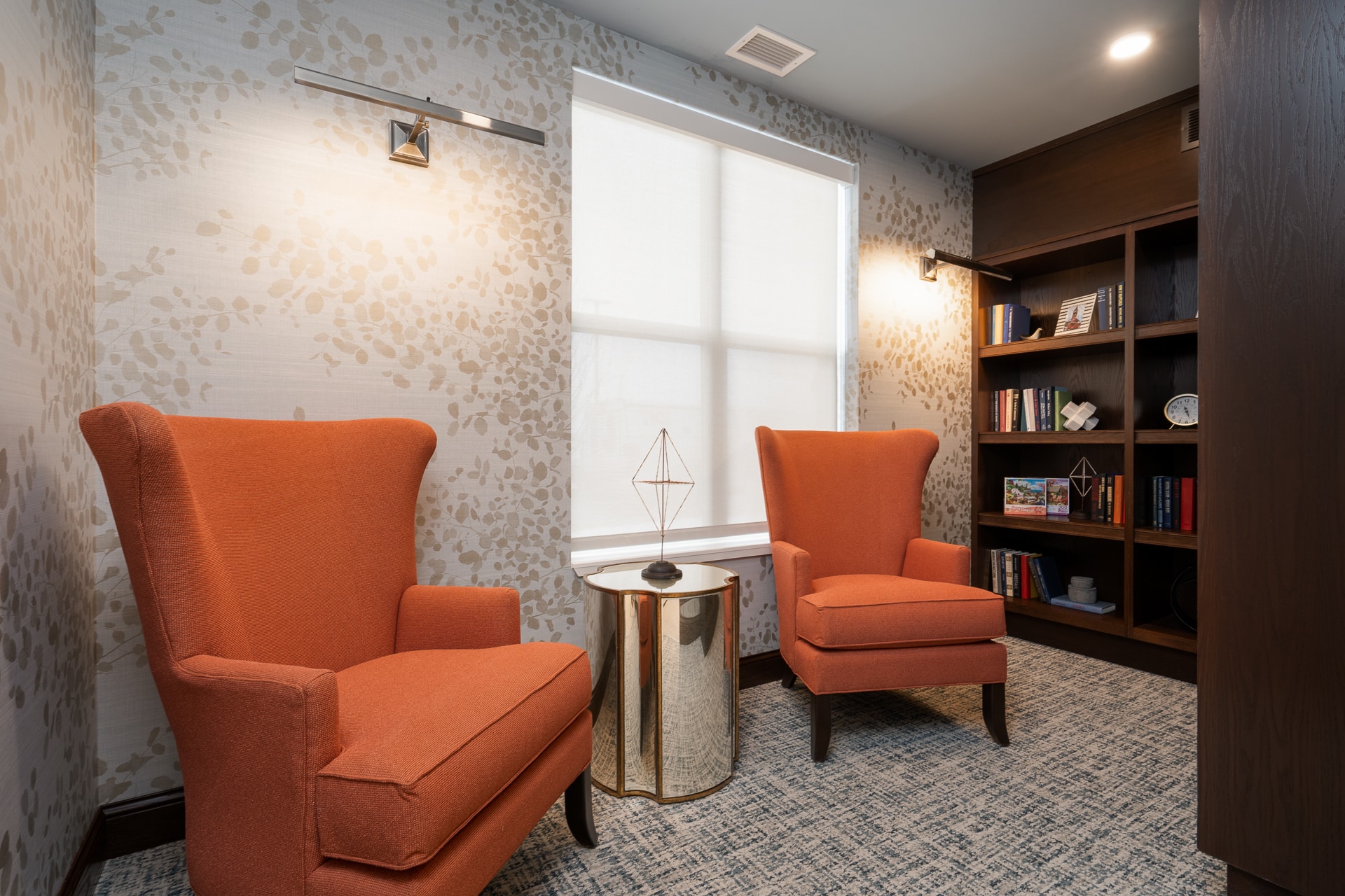 Cozy seating area with orange chairs and bookshelves.