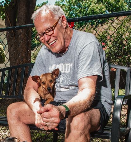 Resident smiling with a small dog outdoors.
