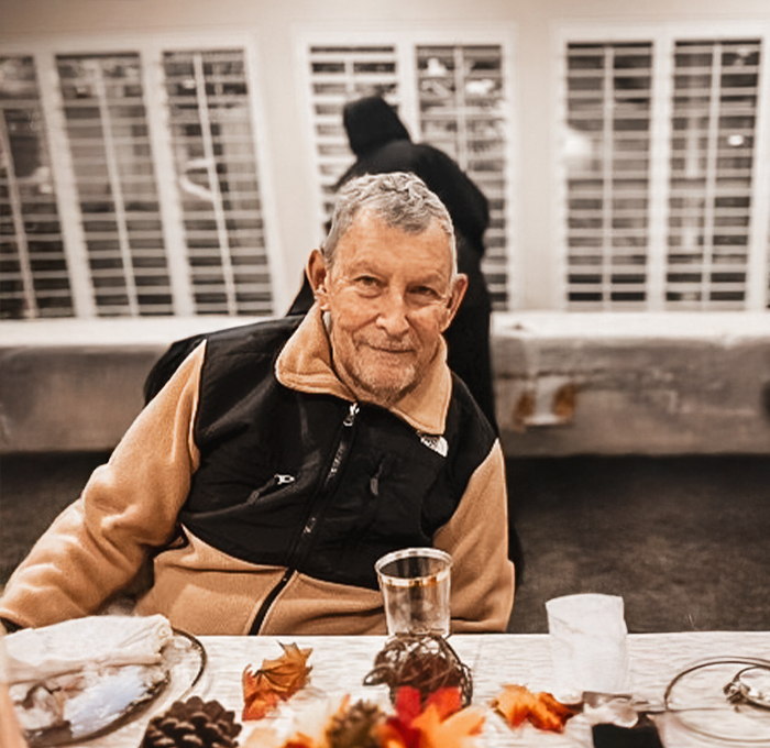 Older man smiling at a dining table setting.