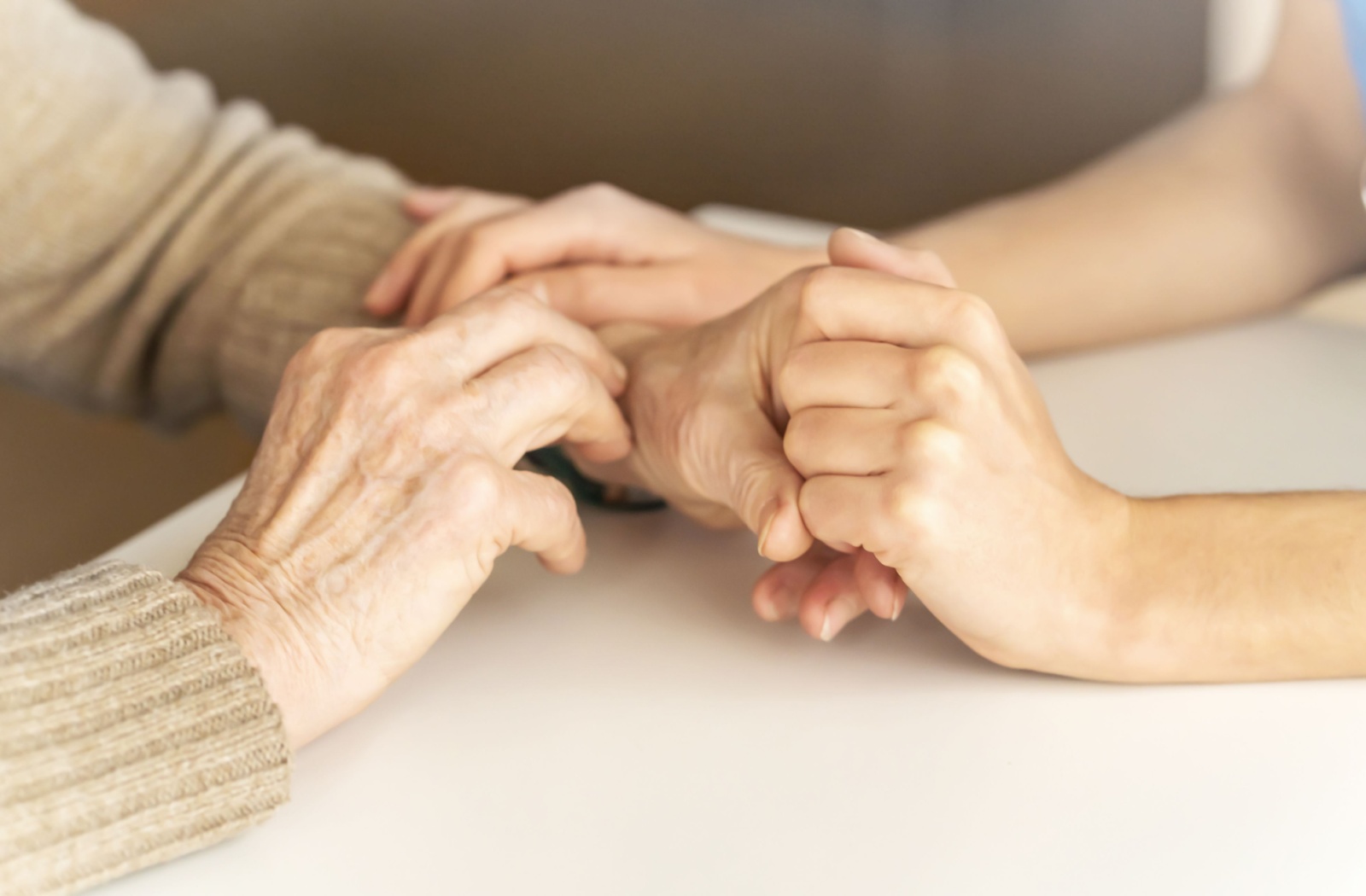 Elderly and caregiver hands in a supportive gesture.
