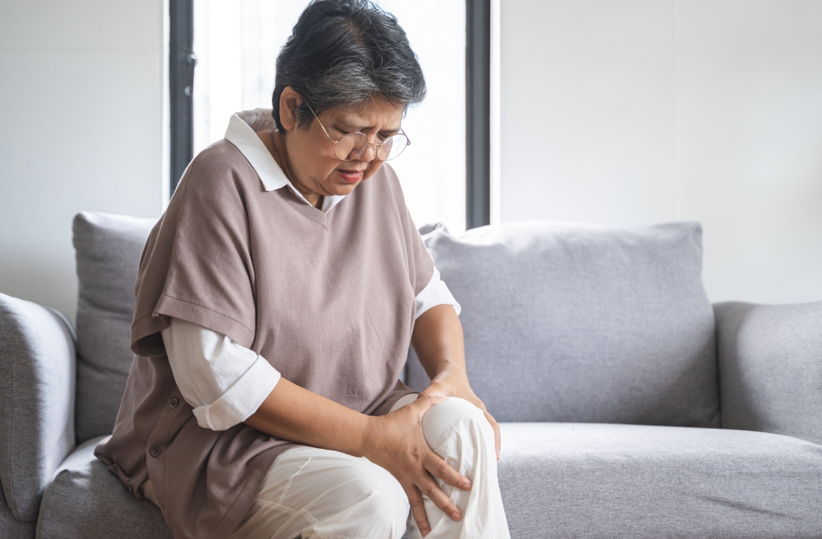 Senior woman sitting on couch, holding her knee.