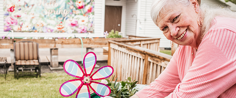 Senior woman gardening outdoors with a colorful flower decoration.