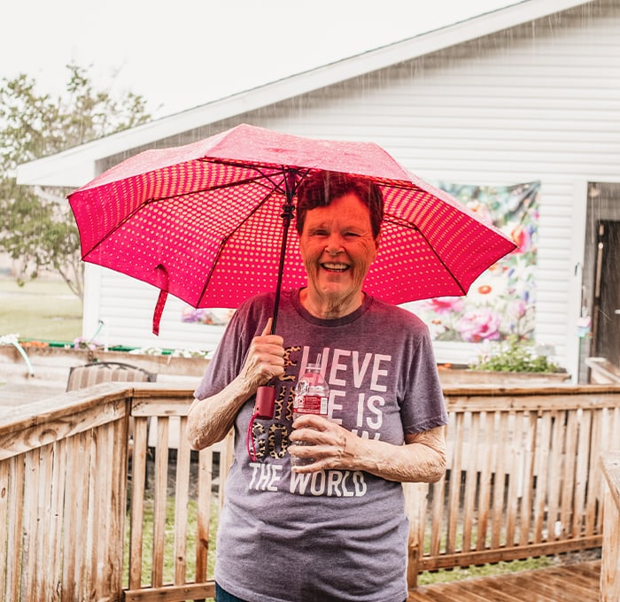 Senior woman smiling under a pink umbrella outside