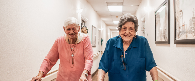 Two smiling residents walking in a hallway.