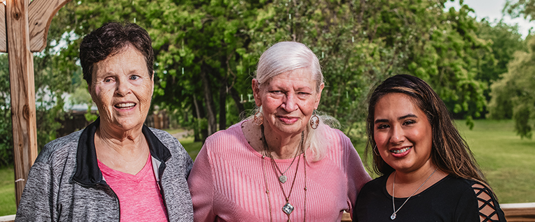 Three women smiling outdoors in a garden setting.