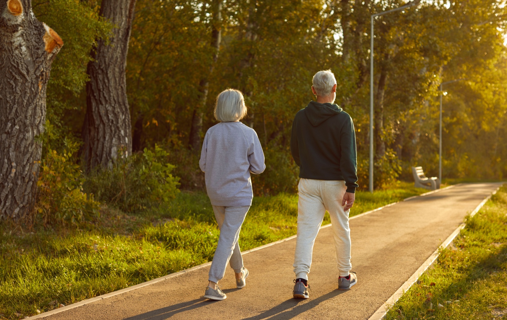 Two seniors walking on a path in a park.