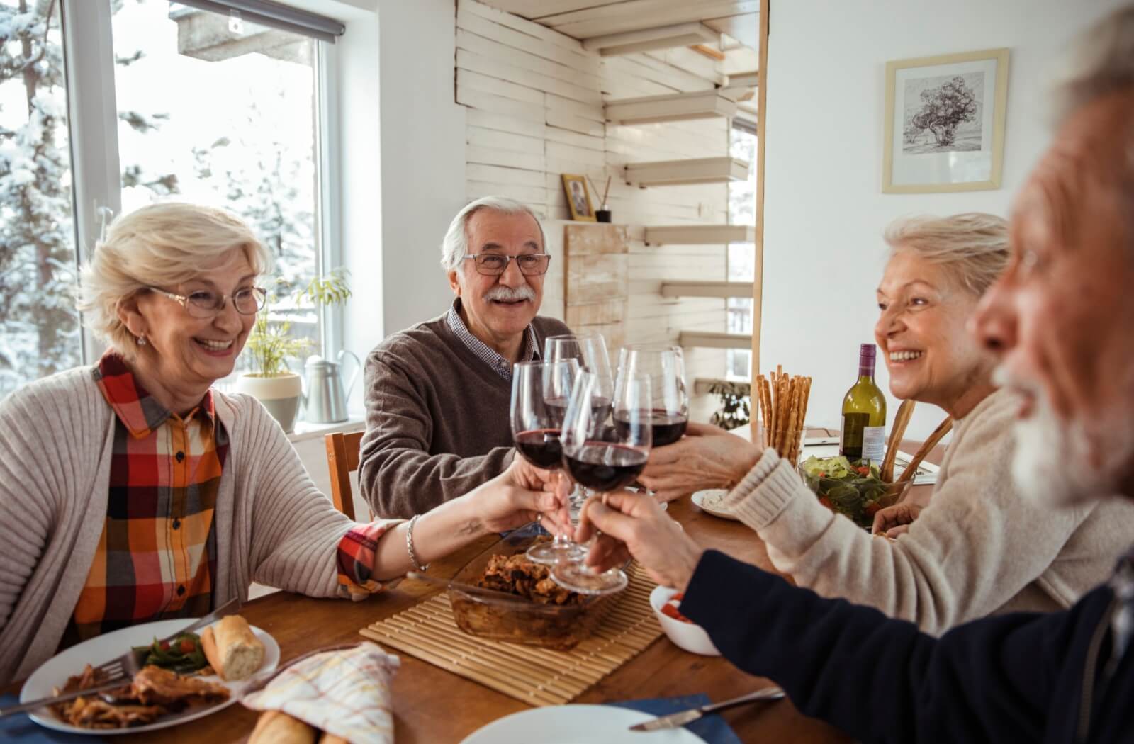 Seniors toasting with glasses of wine at a dining table.