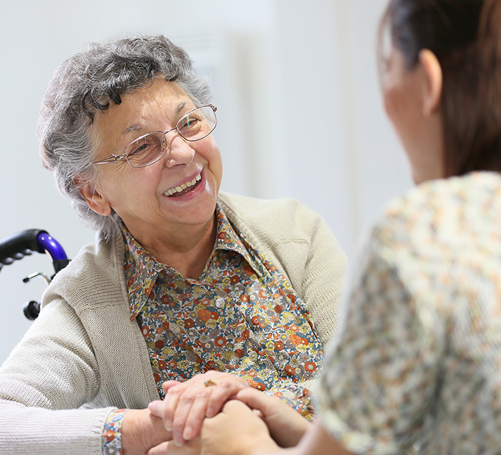 Smiling elderly woman holding hands with caregiver