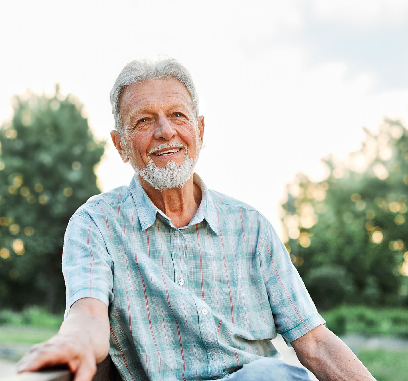 Smiling senior man outdoors with trees in the background.