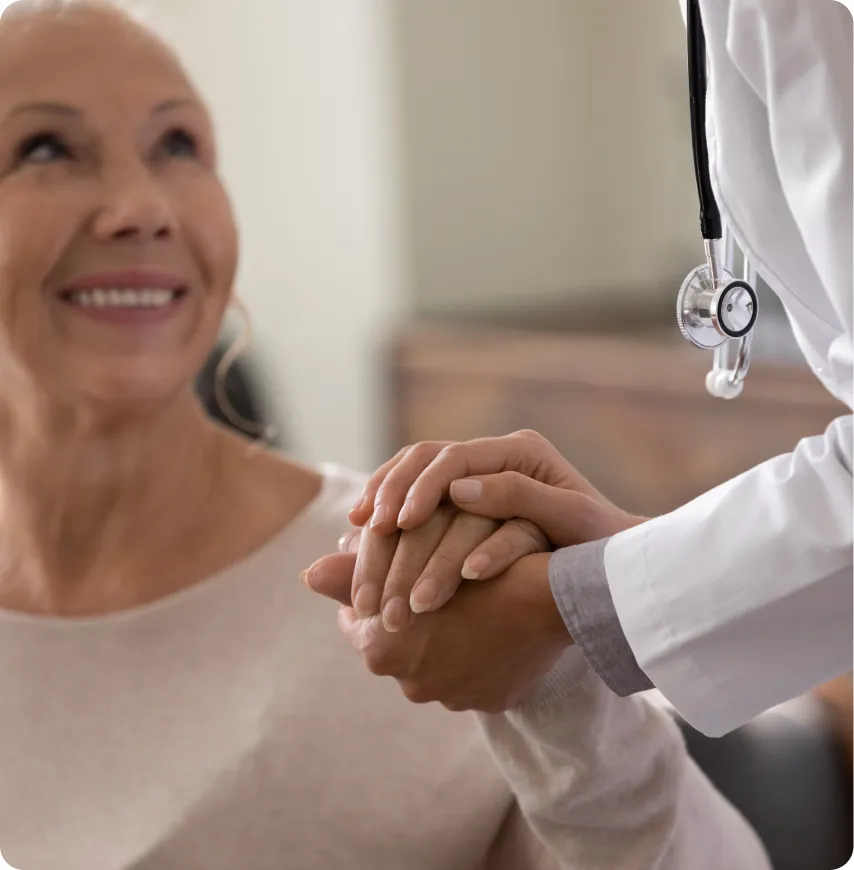 Senior woman smiling while holding hands with caregiver.