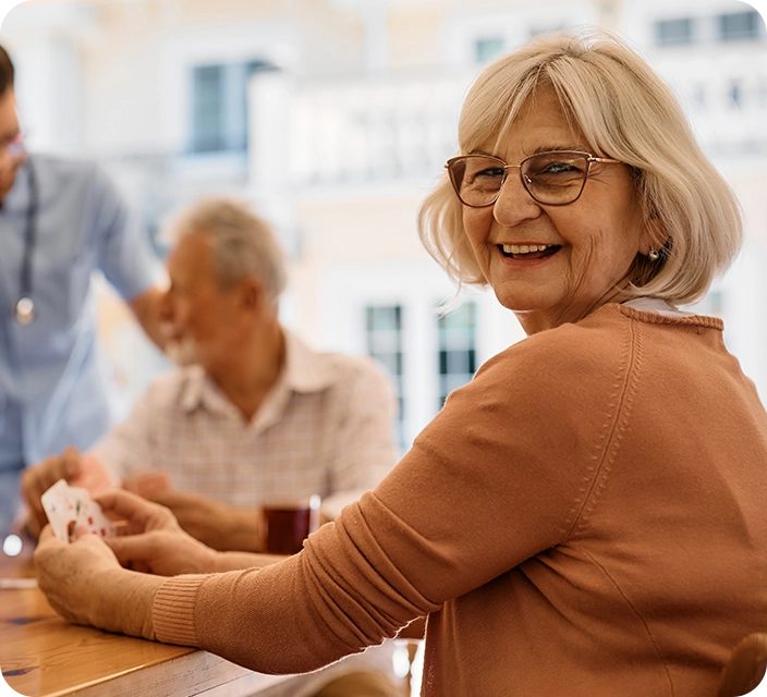 A smiling elderly woman playing cards with others.