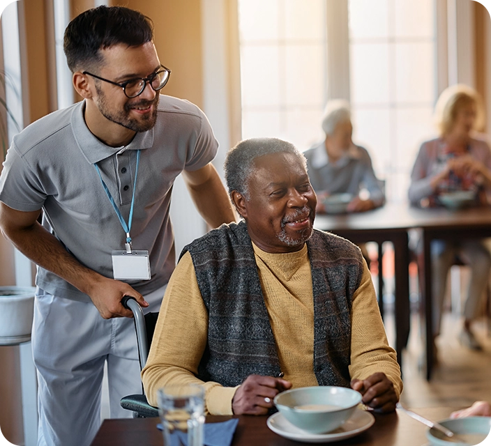 Staff assisting a smiling resident during mealtime.