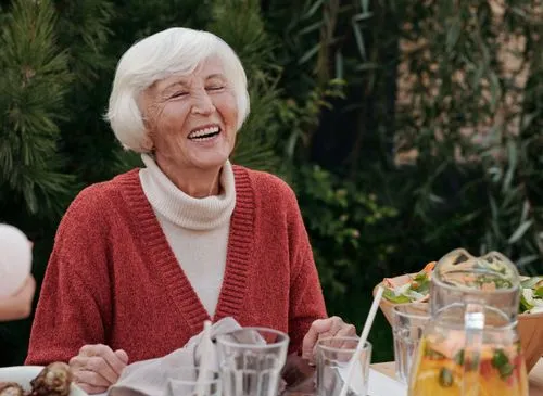Smiling elderly woman enjoying a meal outdoors.