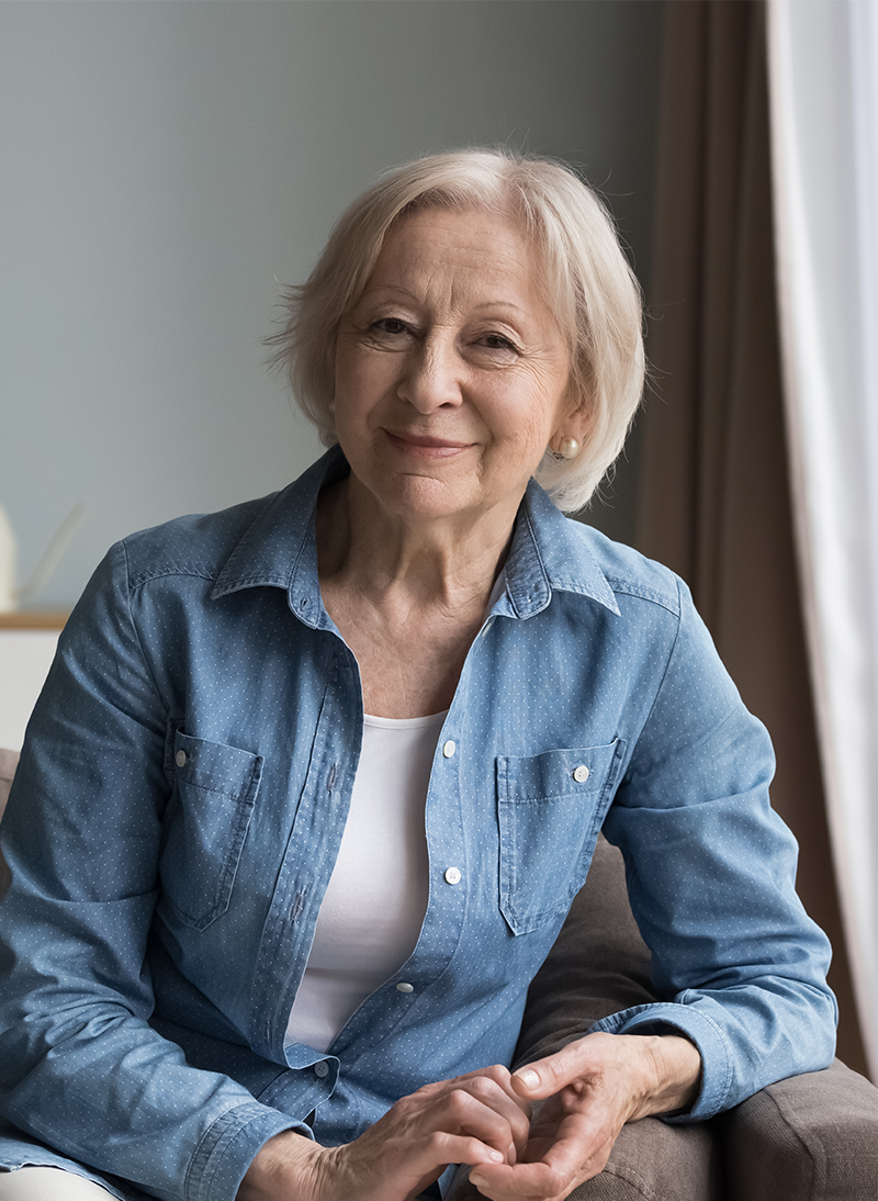Senior woman smiling warmly while sitting indoors.