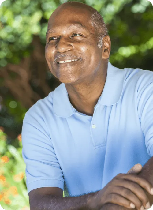 Smiling senior man outdoors with greenery.