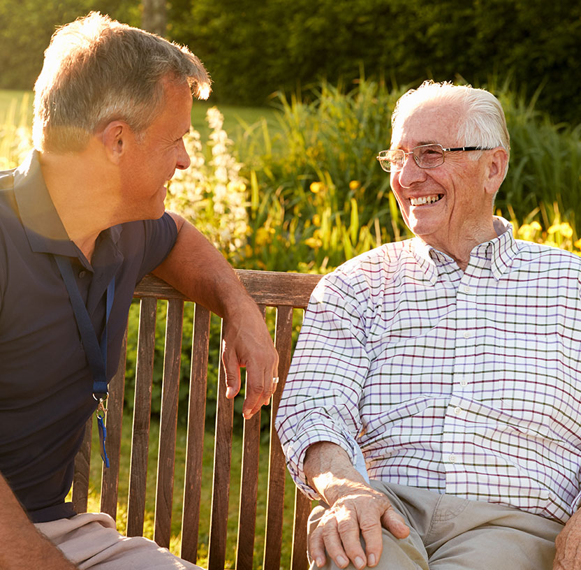 A caregiver and senior man sharing a moment outdoors.
