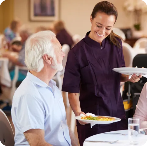 Staff serving a meal to a resident in the dining area.