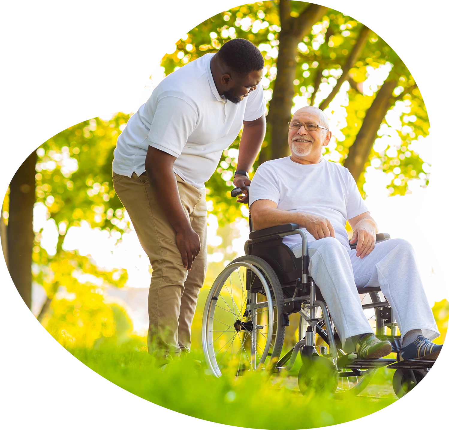 Caregiver assisting an elderly man in a wheelchair outdoors.