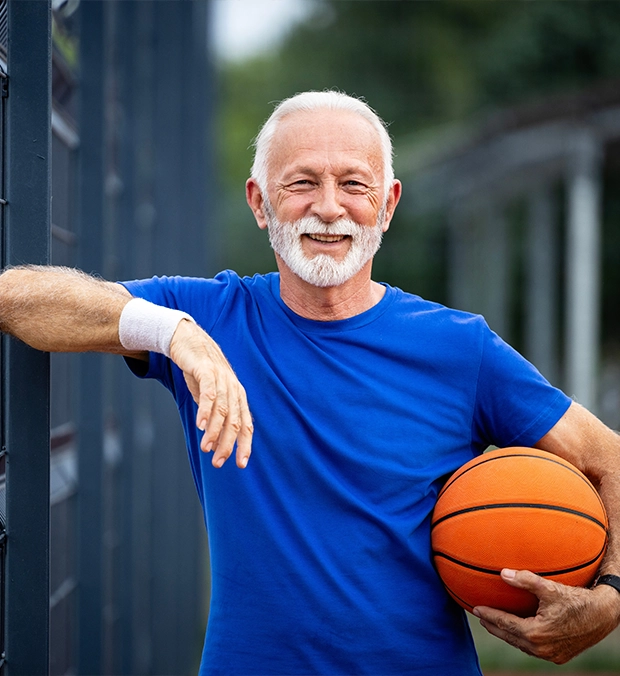 Smiling elderly man holding a basketball outdoors.