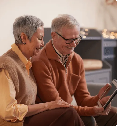 Two seniors joyfully using a tablet together.