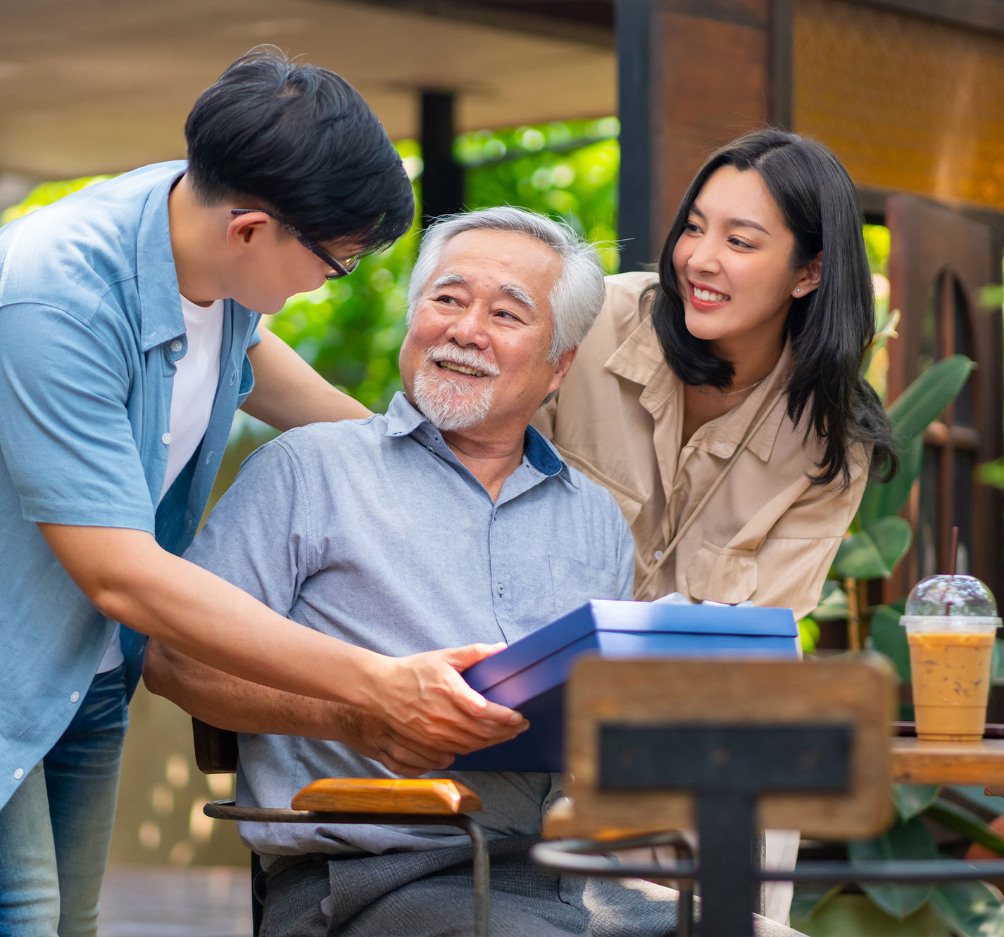 A senior man receiving a gift outdoors from family members