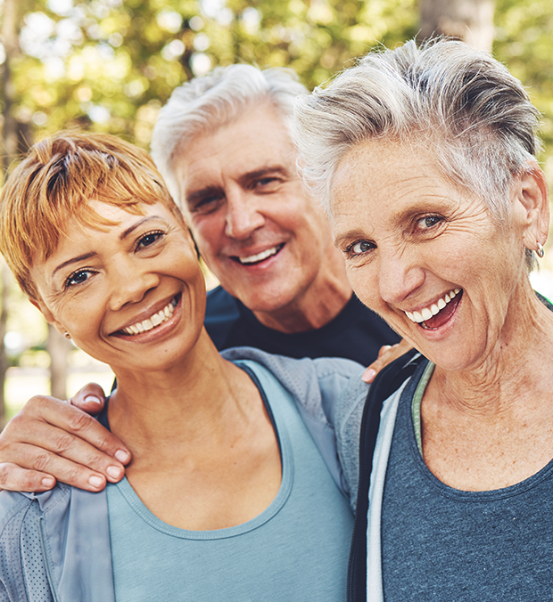 Three smiling residents outdoors in a park setting.