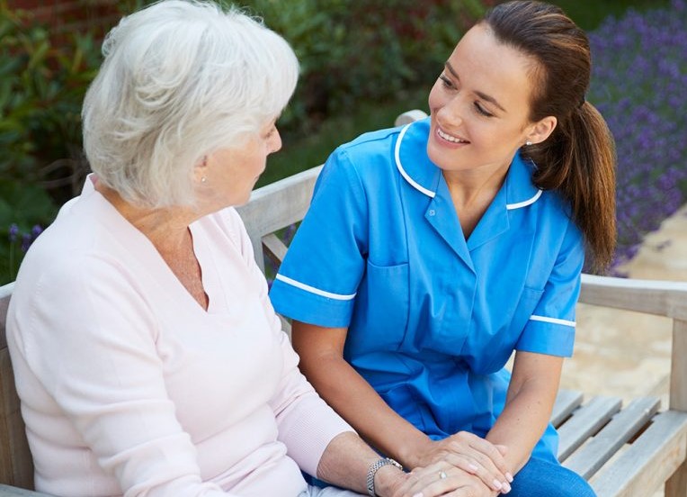 Nurse conversing with an elderly resident outdoors.