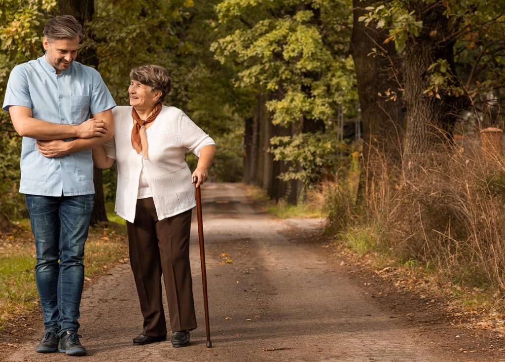 A caregiver and resident walking through a scenic path.