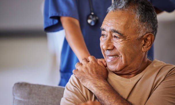Senior man smiling with caregiver's hand on shoulder.