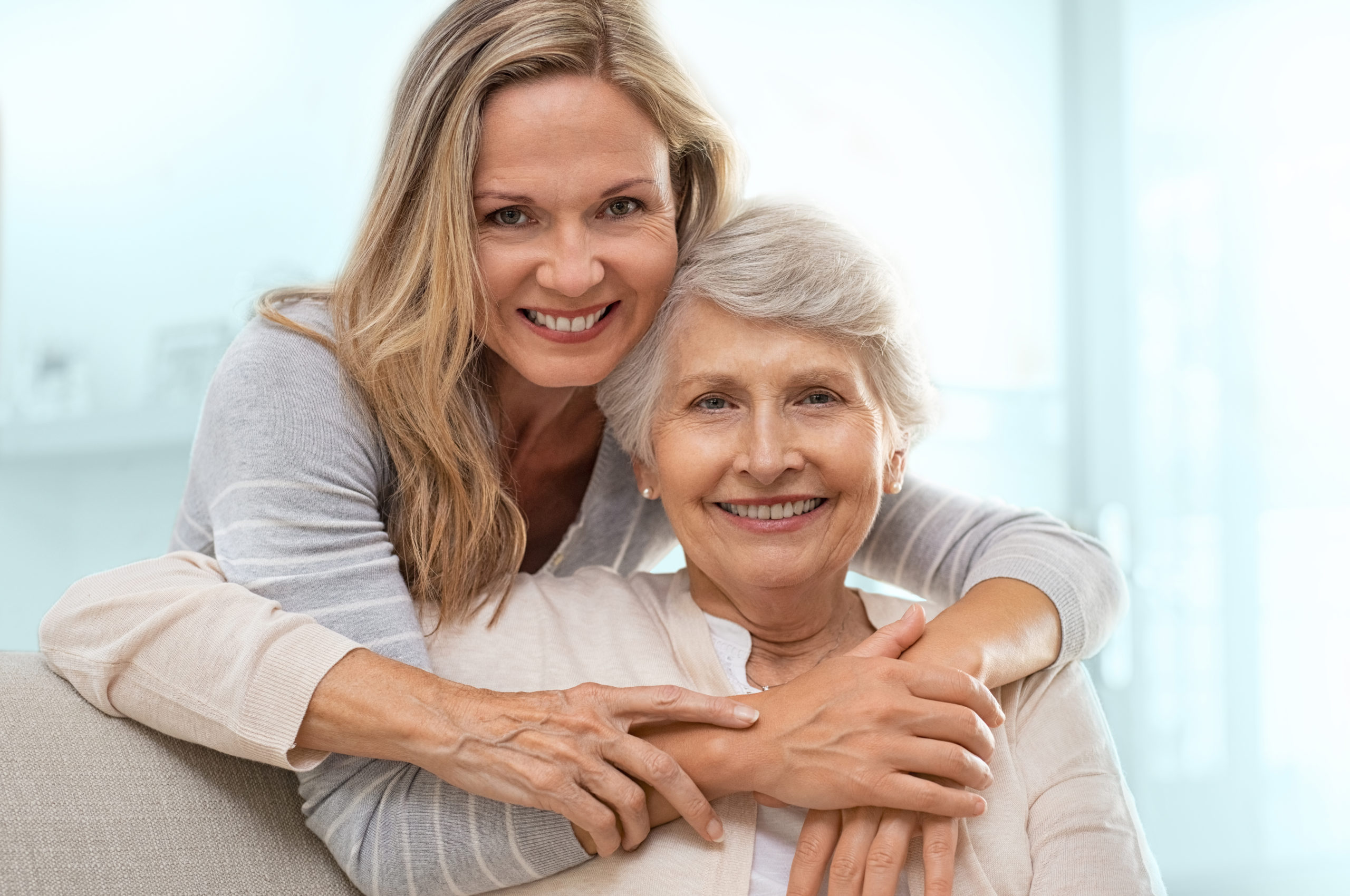 A smiling older woman being embraced by a caregiver