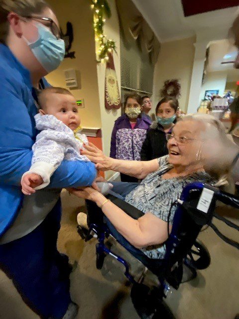 Resident interacting with baby and staff indoors
