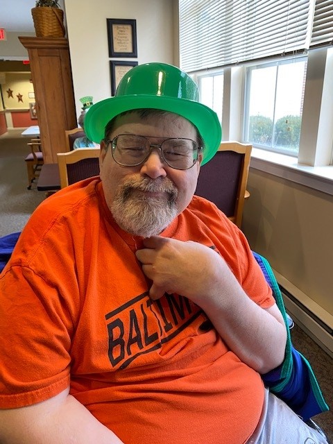 Resident wearing a green hat, smiling indoors.
