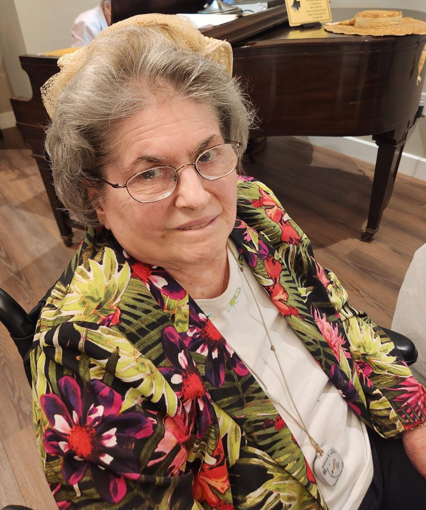 Senior resident in a floral jacket seated indoors.