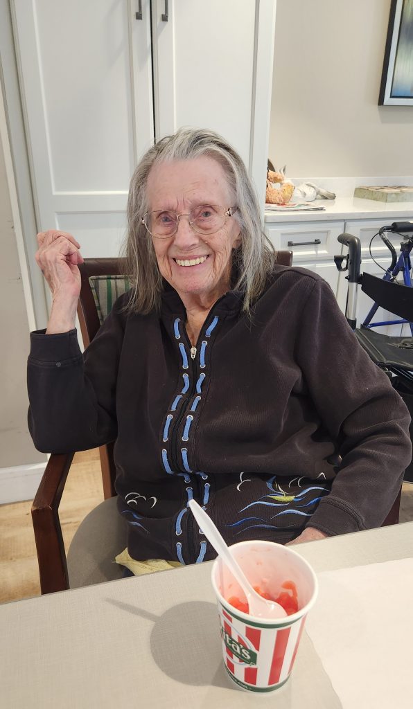 Smiling elderly woman with dessert in a dining area.