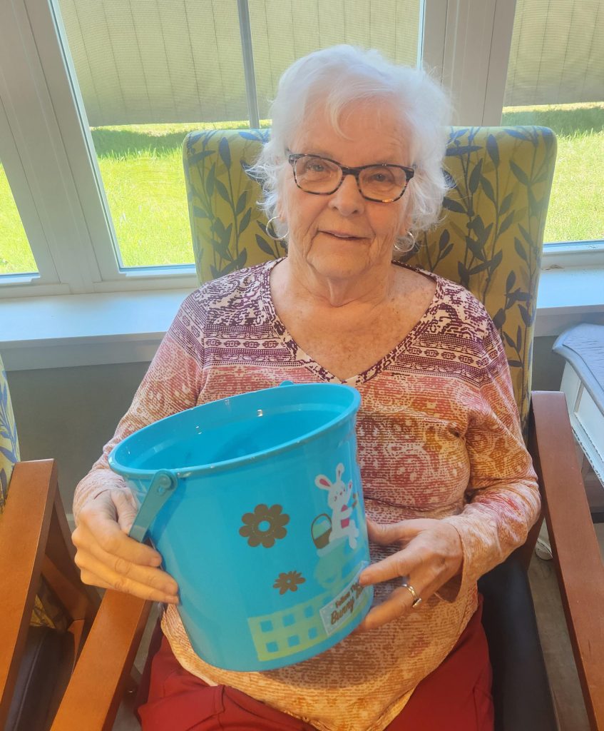 Senior resident holding a colorful bucket in a bright room.