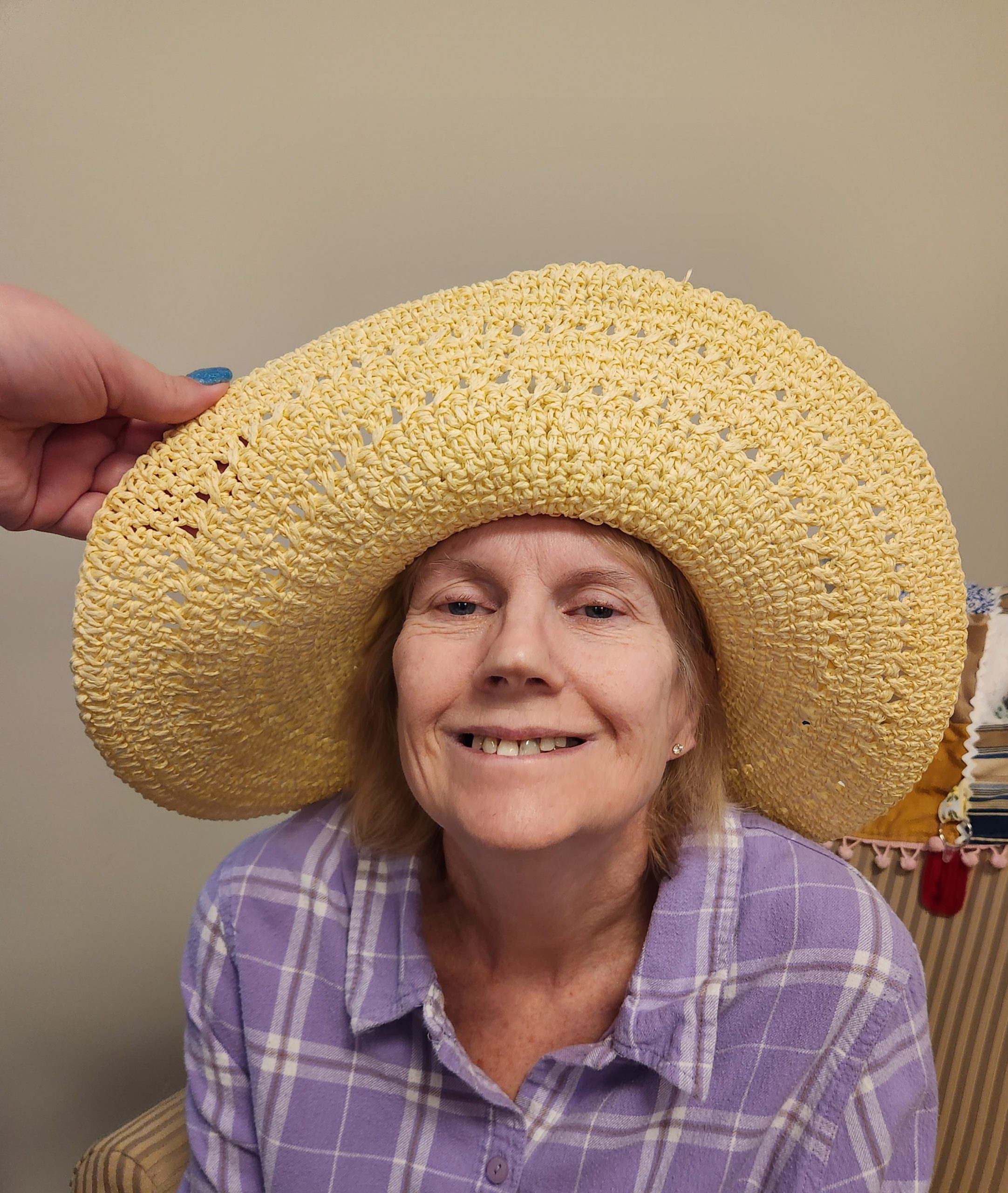 Senior woman smiling while wearing a large straw hat.