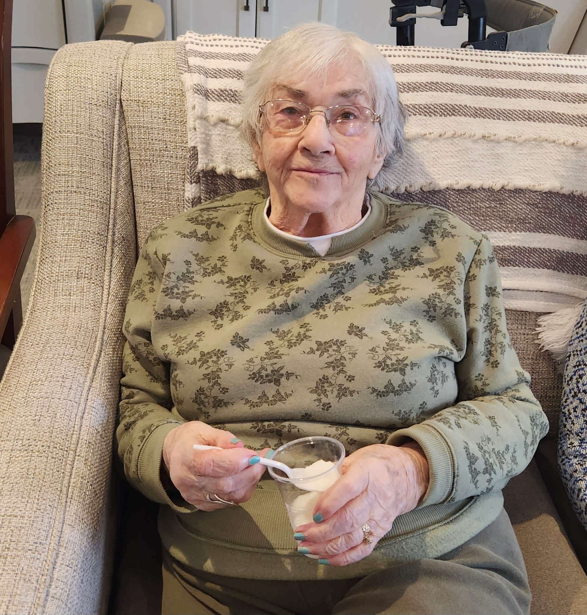 Senior resident enjoying dessert on a couch.