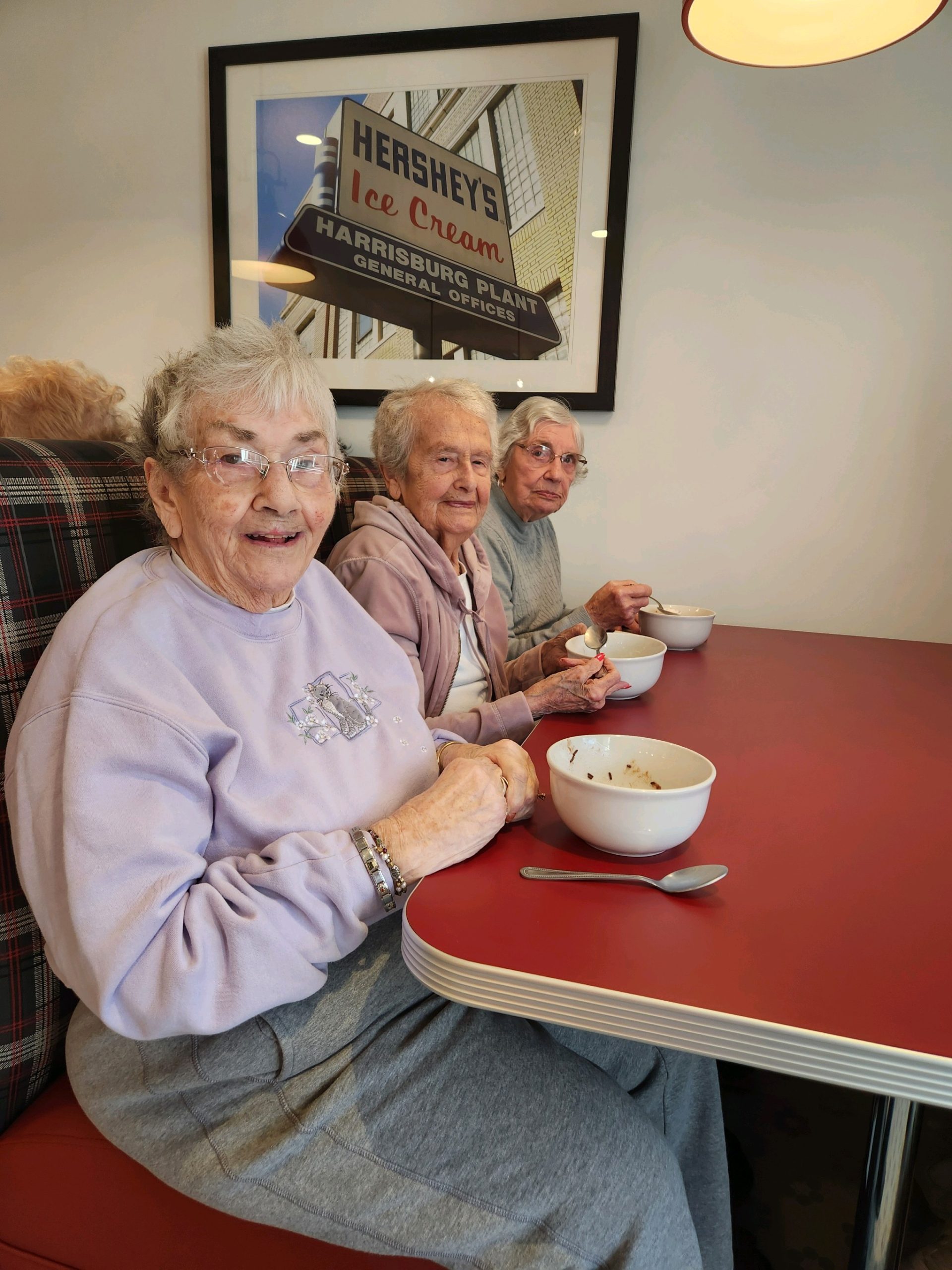 Three elderly women enjoying ice cream in a dining area.