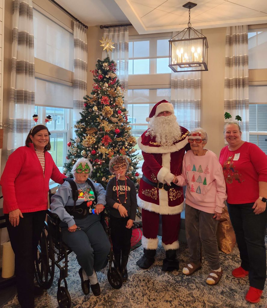 Residents and staff celebrating with Santa near a Christmas tree.
