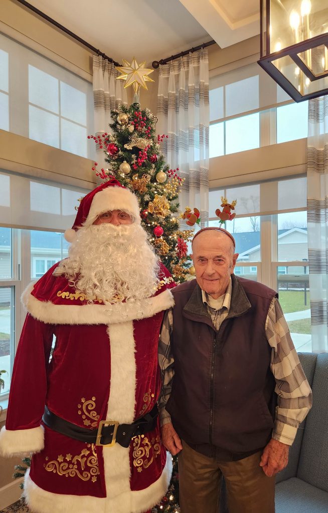Resident poses with Santa by decorated Christmas tree.