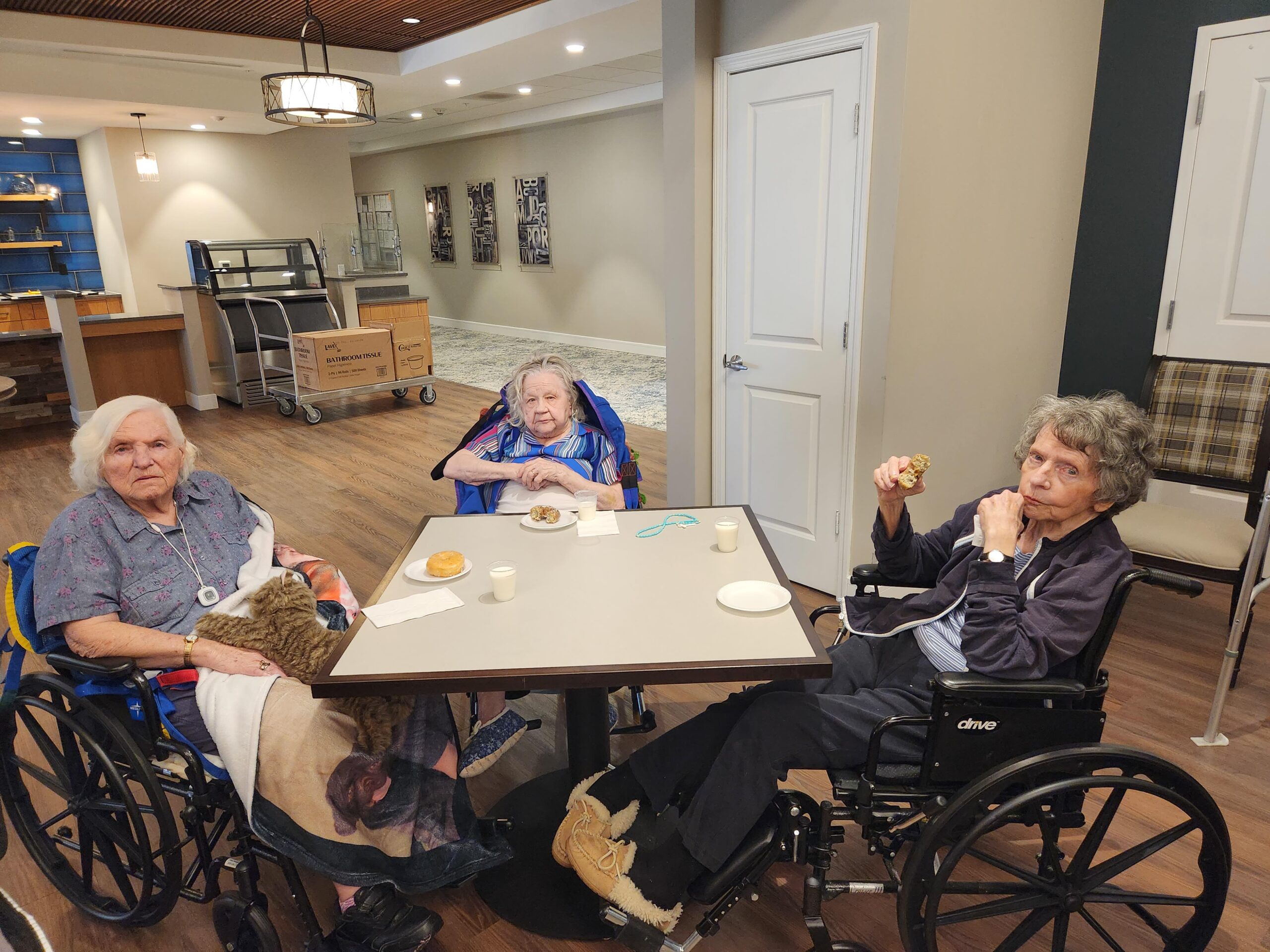Three elderly women sitting around a table with snacks.