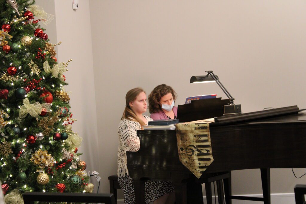 Two women playing piano near a Christmas tree.