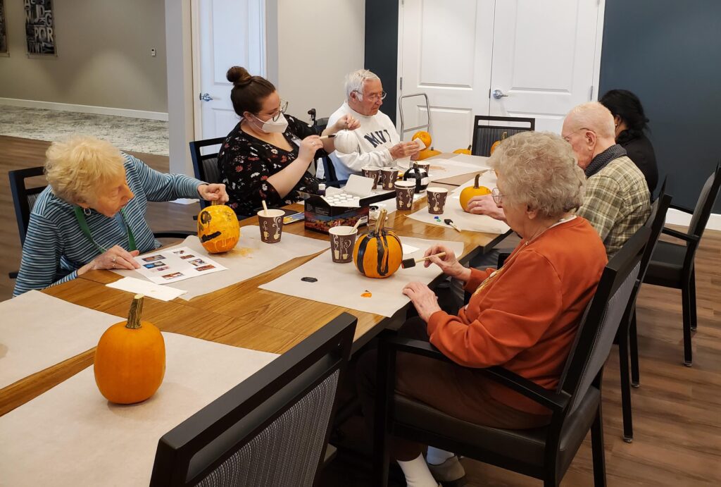 Residents engaged in pumpkin decorating activity indoors.