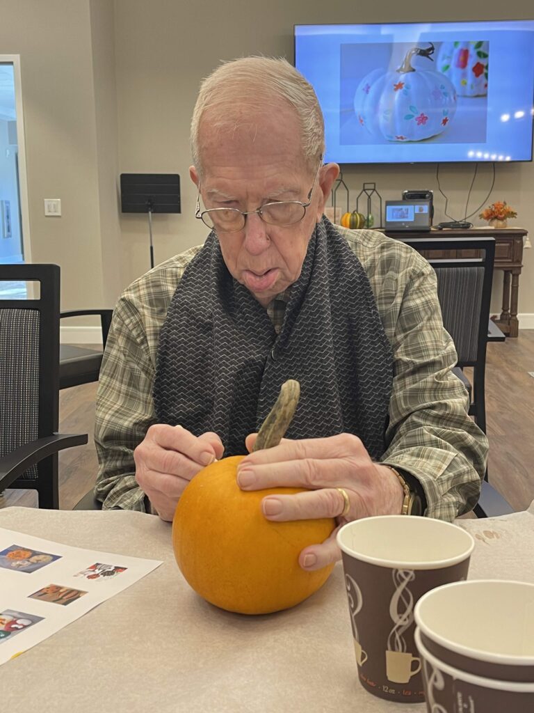 Senior man crafting a pumpkin in a social setting.