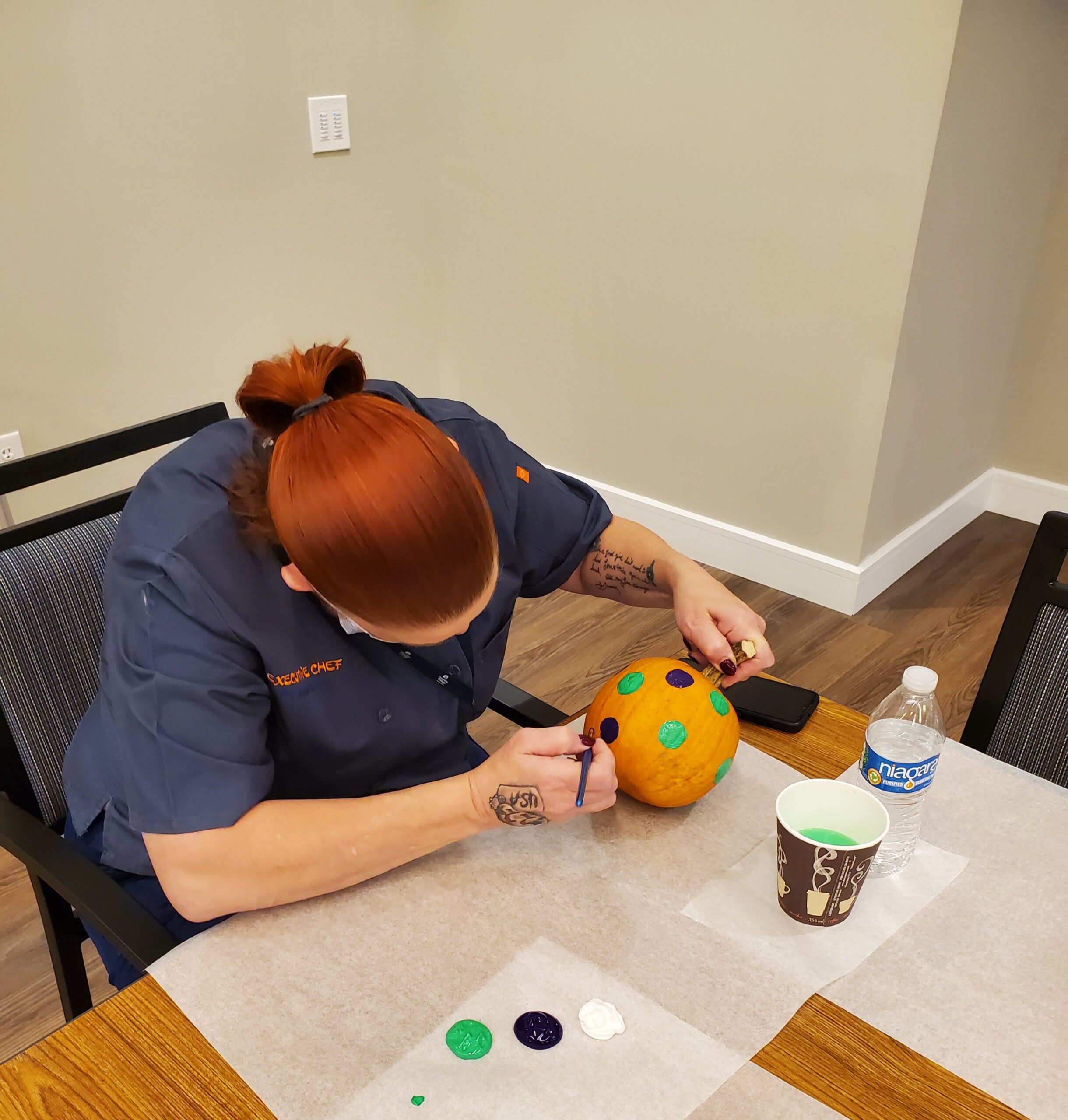 Staff member painting a pumpkin indoors.