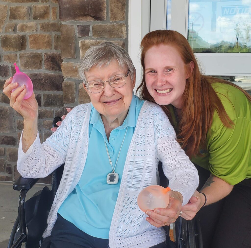 Resident and staff member holding colorful balloons.