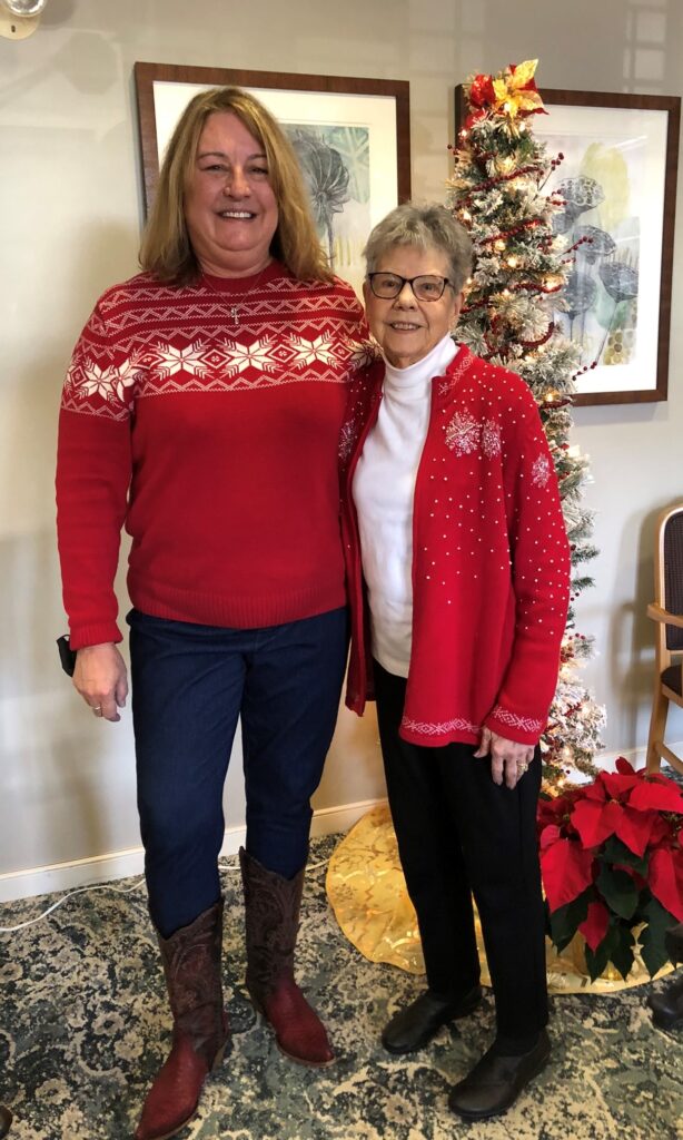 Two women in festive sweaters by a Christmas tree.